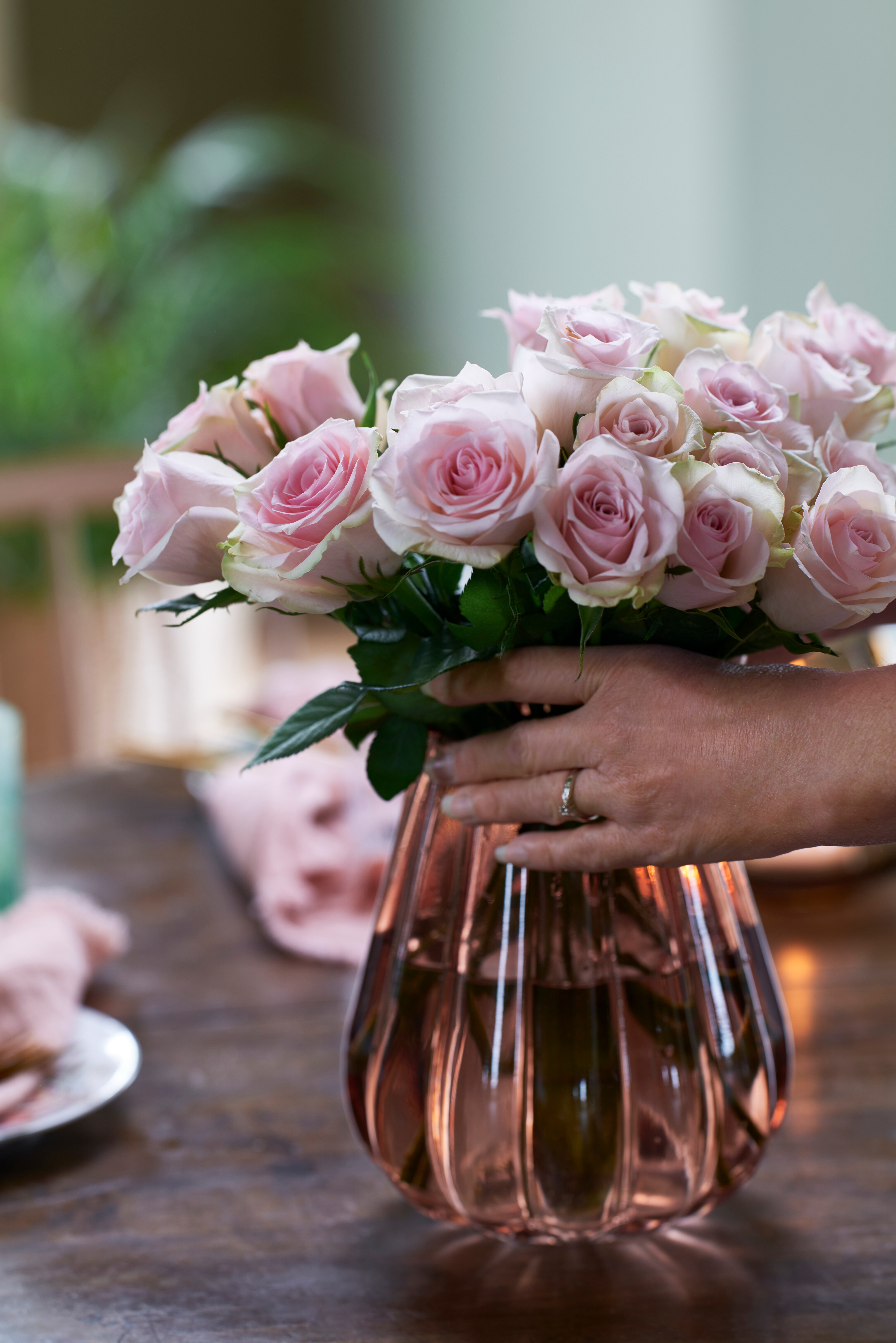 Hender holder en bukett rosa roser i en vase